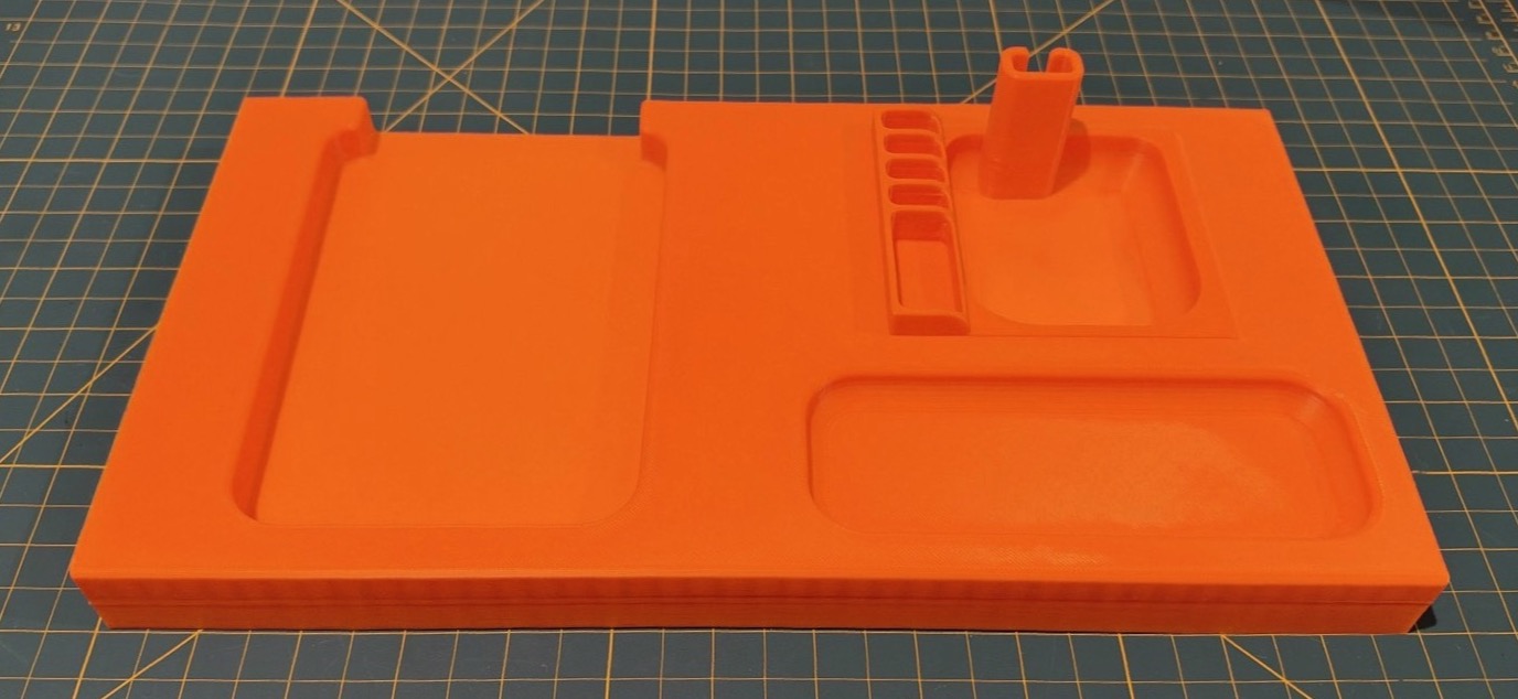 The orange printed tray on a cutting mat, showing a large recess on the left, smaller slots and an upright holder on the right, and a long compartment at the front.