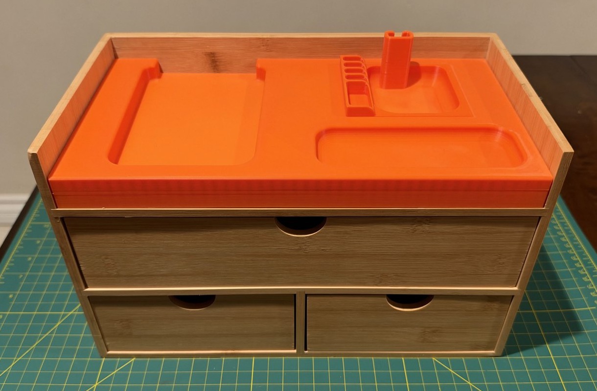 The empty orange organizer fitted into the top of a wooden unit with one wide drawer and two smaller drawers below.
