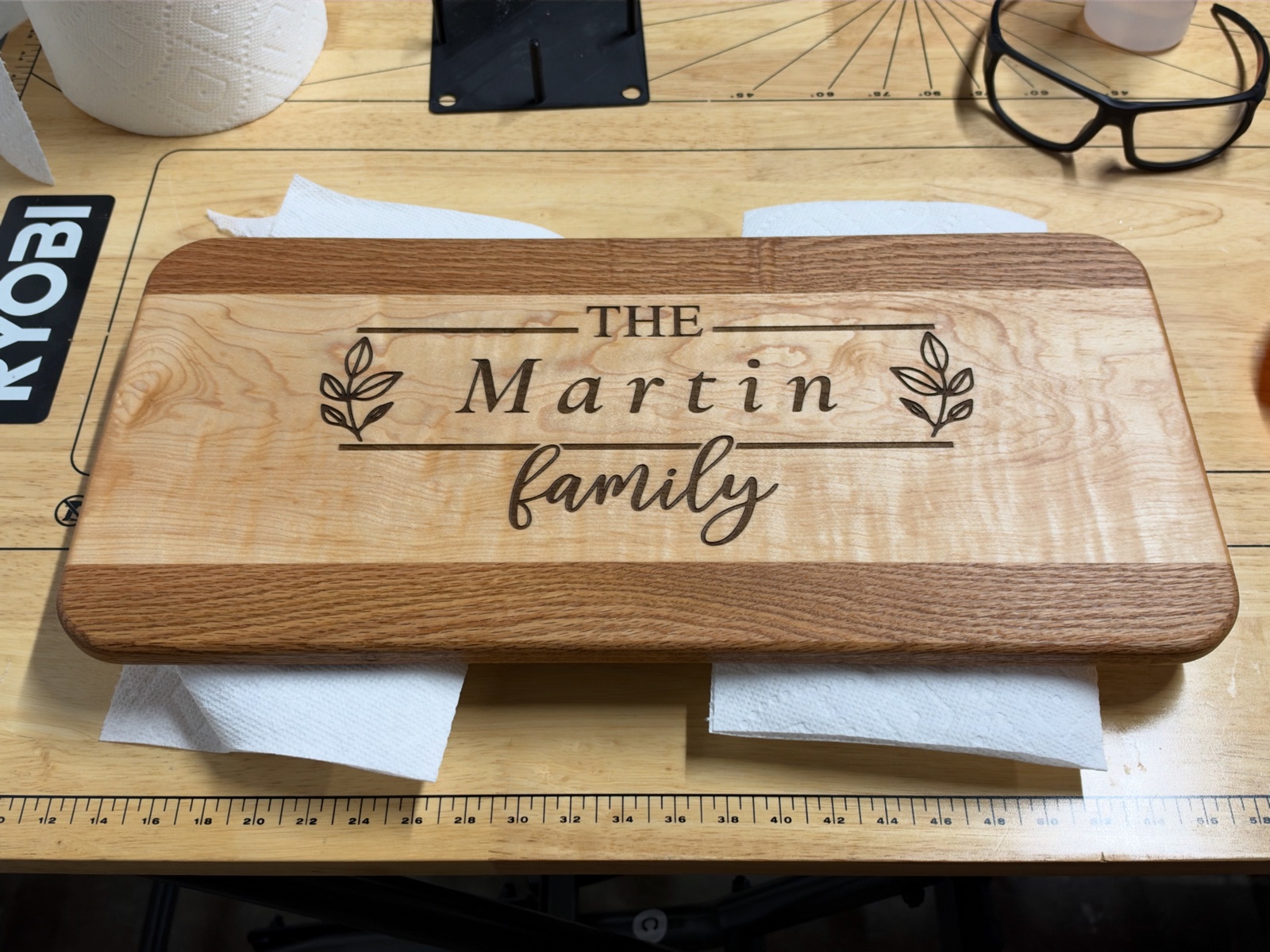 A finished wooden board with rounded corners, contrasting wood strips, and an engraving reading The Martin family, resting on a workshop bench.