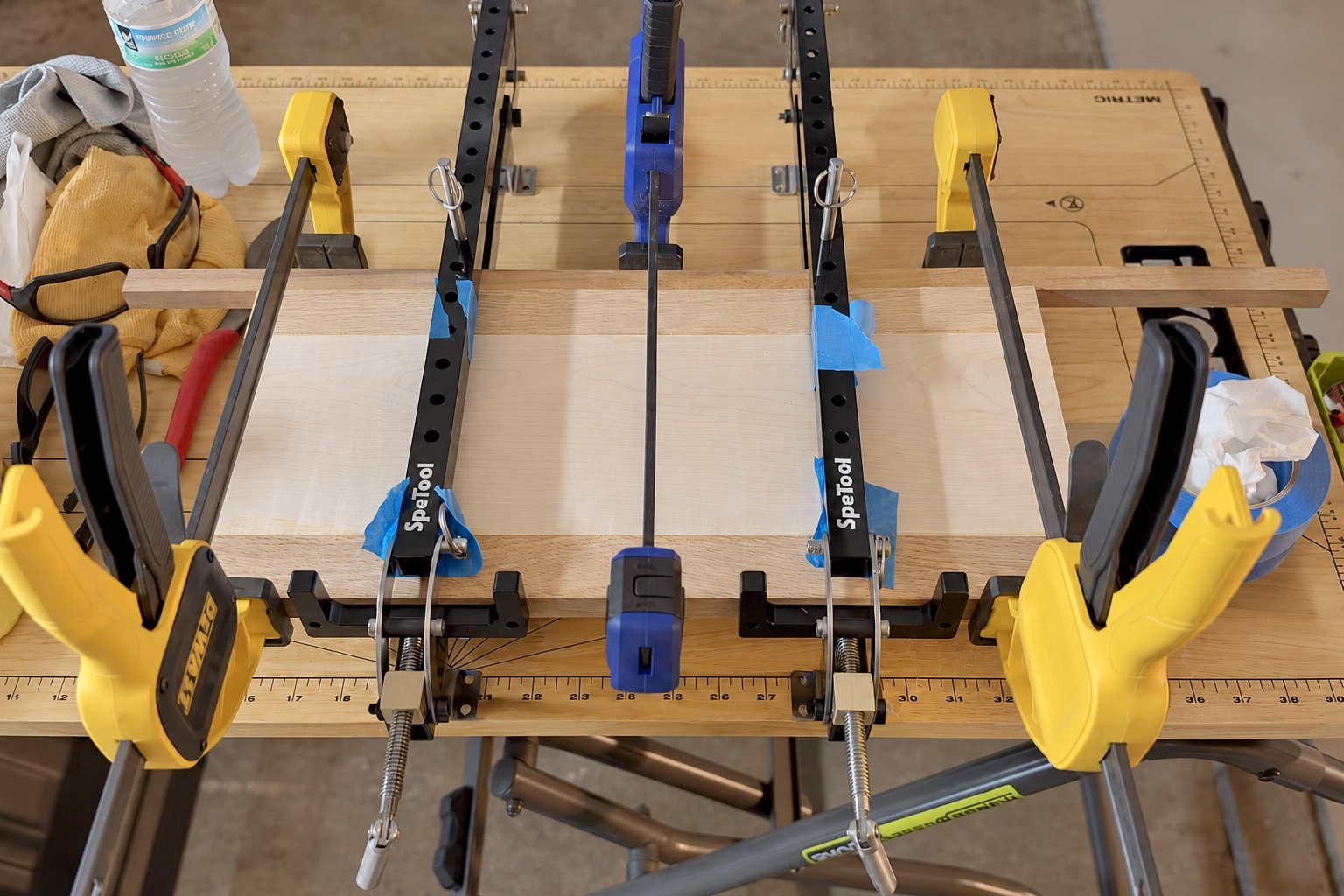 A wooden board glue-up held by several bar clamps on a workshop bench.